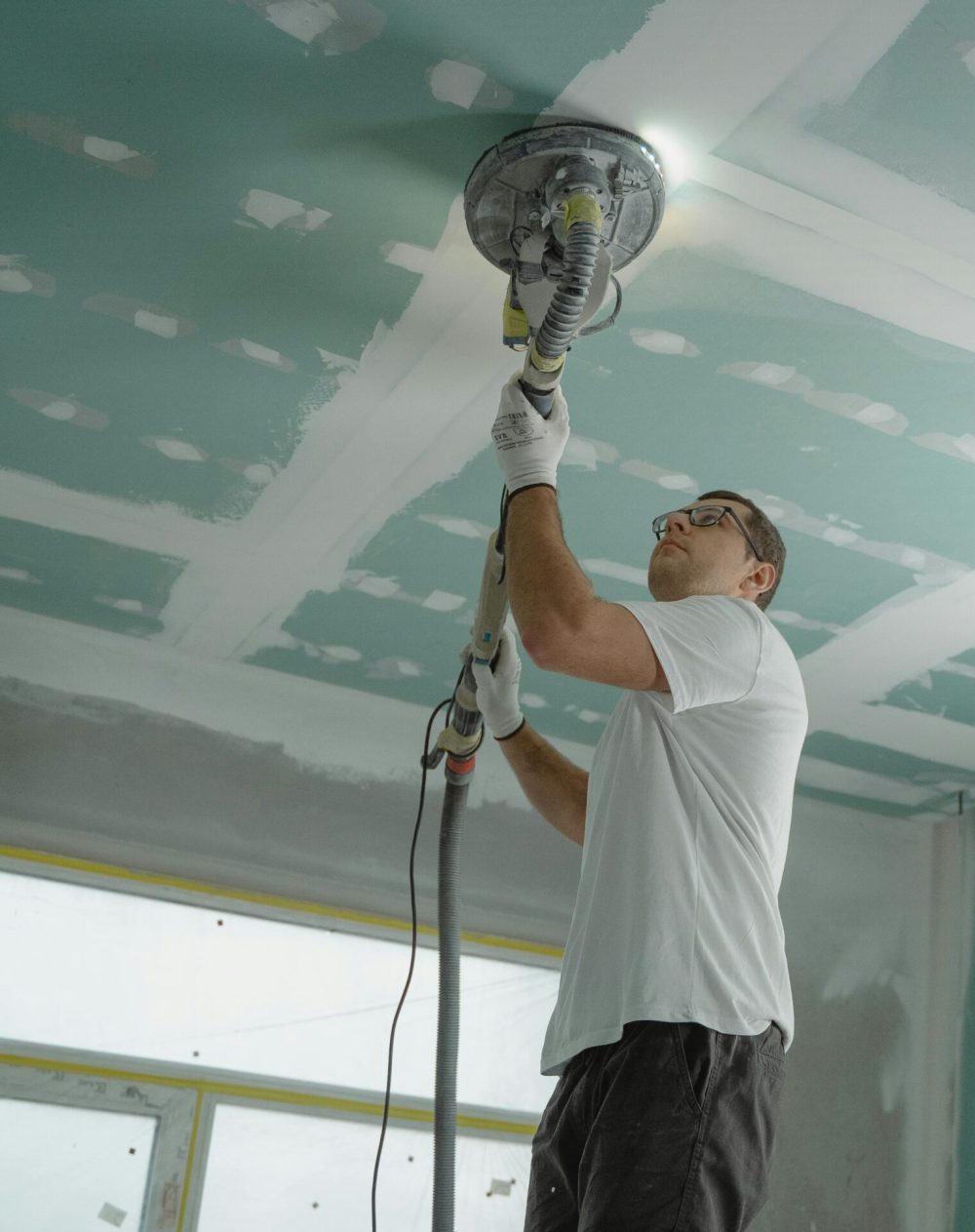 A professional worker sanding the ceiling during a home renovation project. Indoor construction setting.