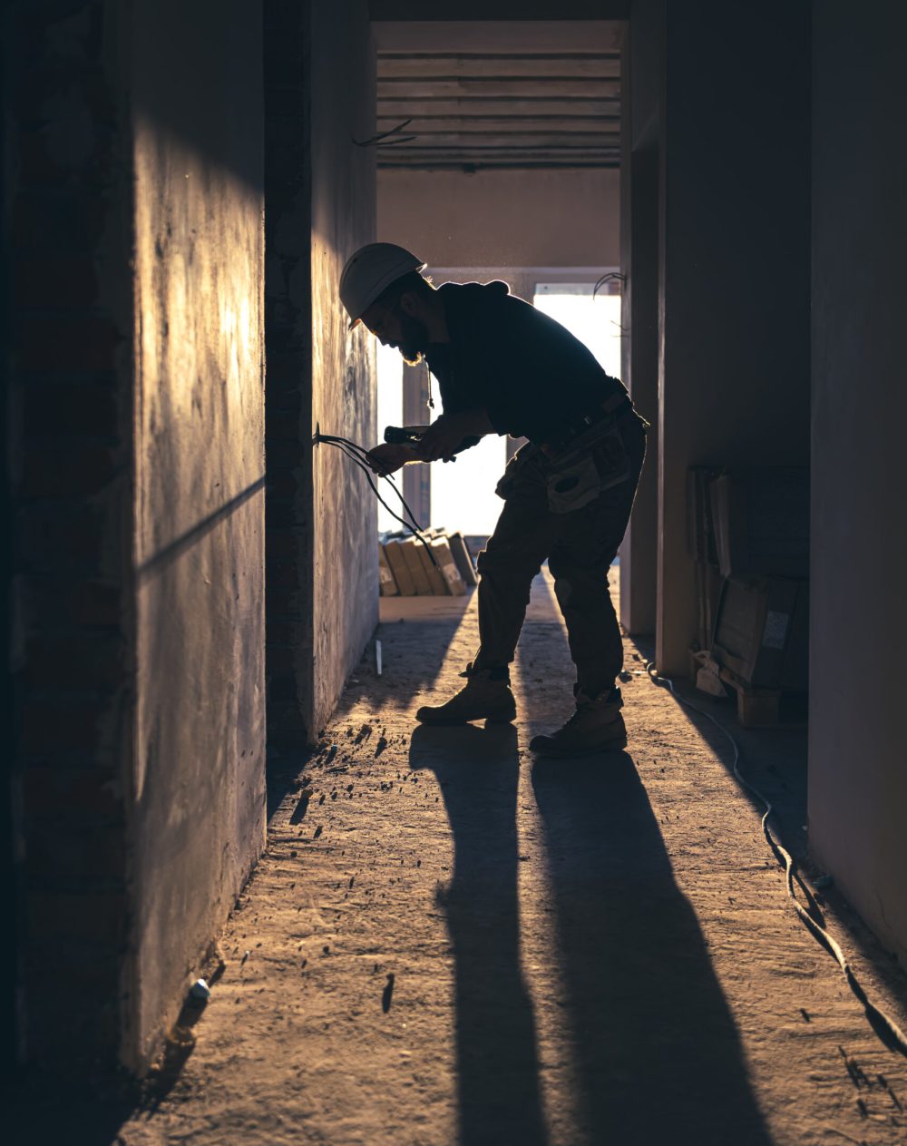 A construction electrician cuts a voltage cable during a repair, silhouette in the light of the setting sun.